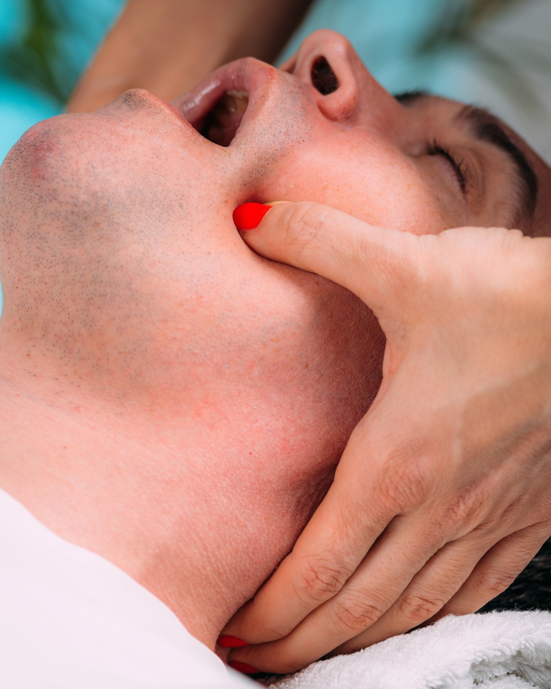Rééducation maxillo-faciale : une main accompagne la mâchoire d’un patient allongé, bouche ouverte.